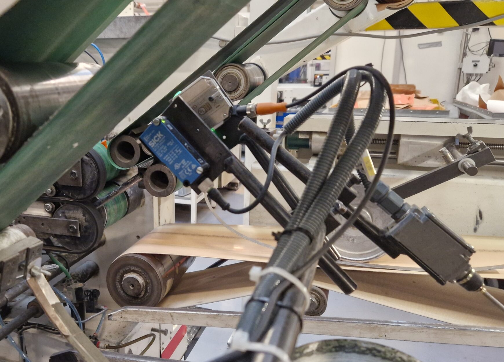 Close-up of an industrial sensor mounted on a CNC machine's conveyor rollers to monitor material flow and production timing.
