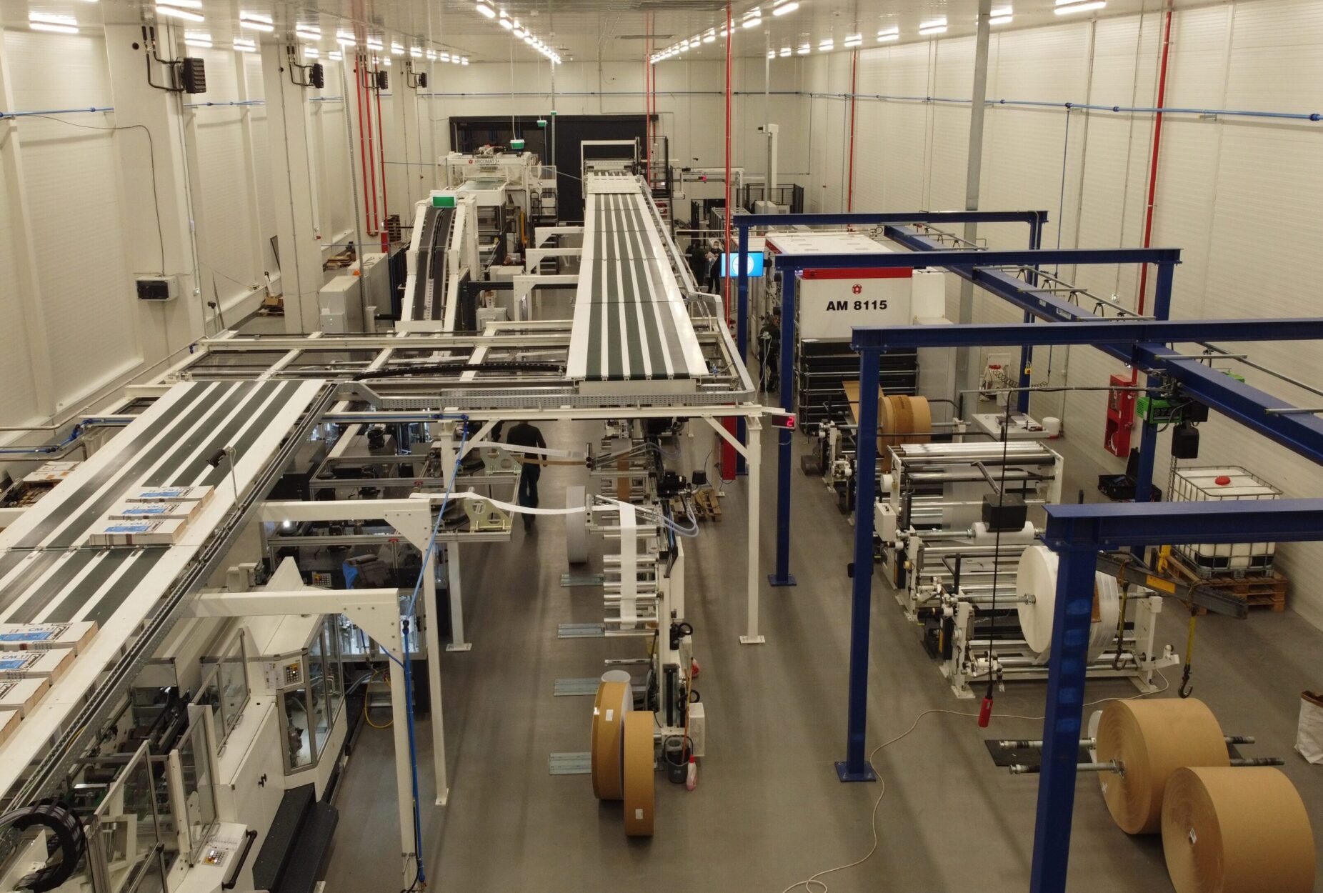 High-angle view of the Advanced Industries Packaging (AIP) production floor in Romania, showing large-scale paper rolls and automated packaging machinery.